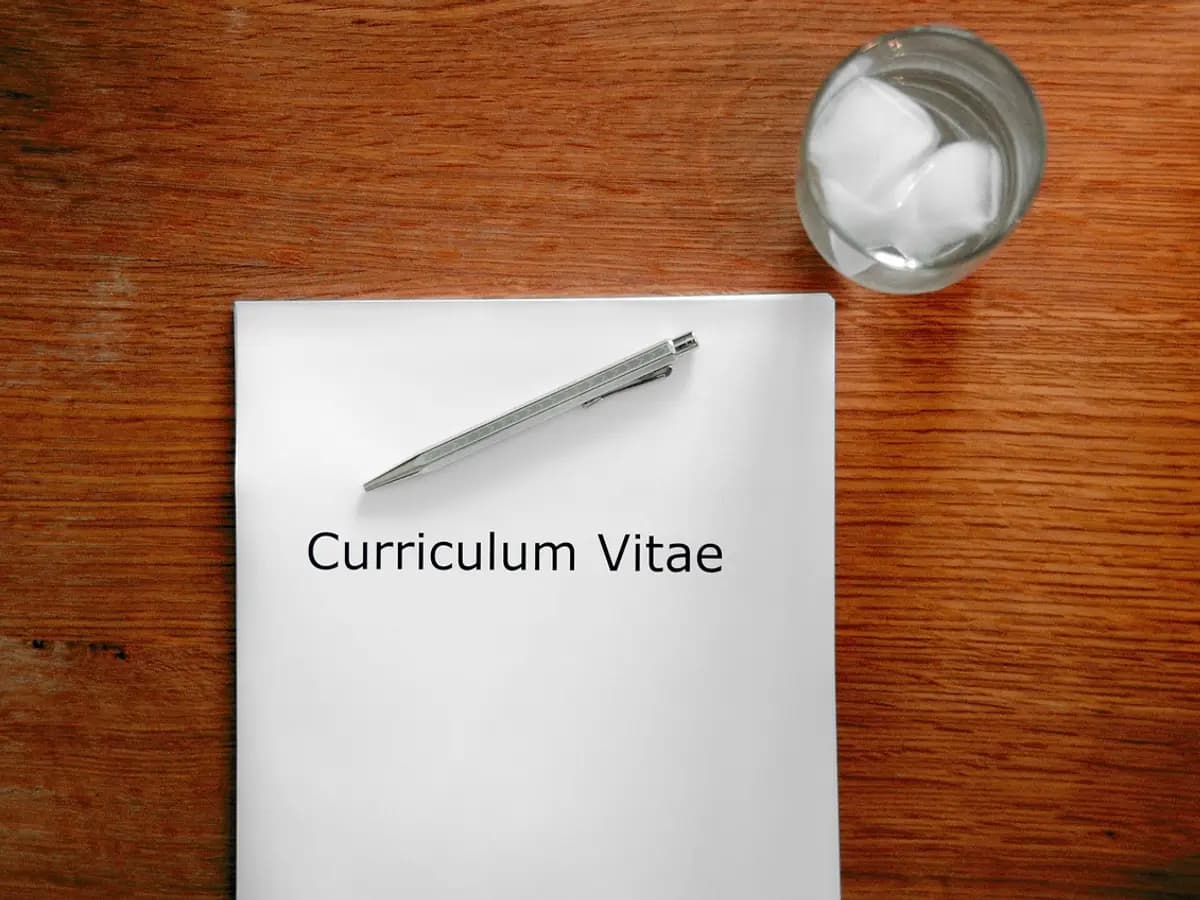 A printed curriculum vitae with a pen on a wooden desk, beside a glass of water