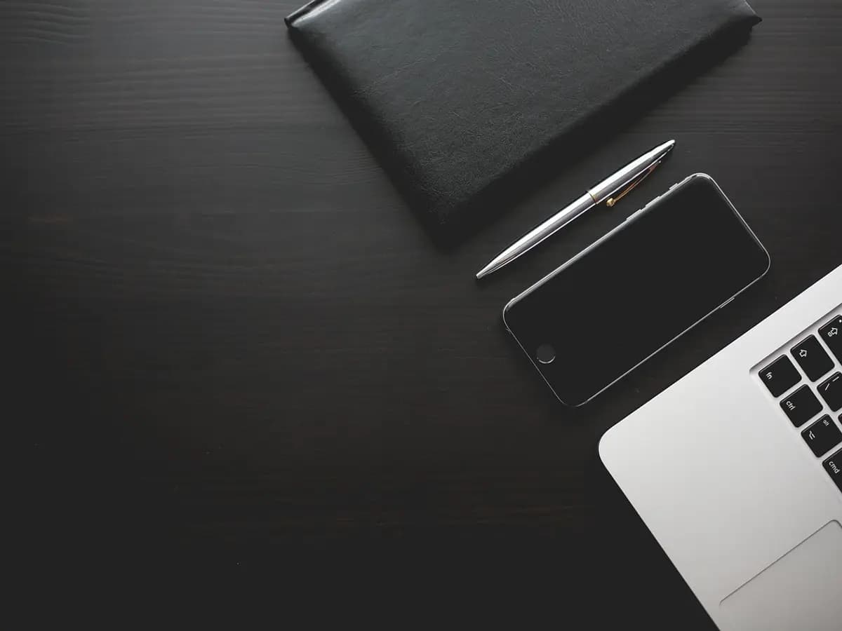 A black smartphone lying face down beside a laptop and a pen on a dark desk