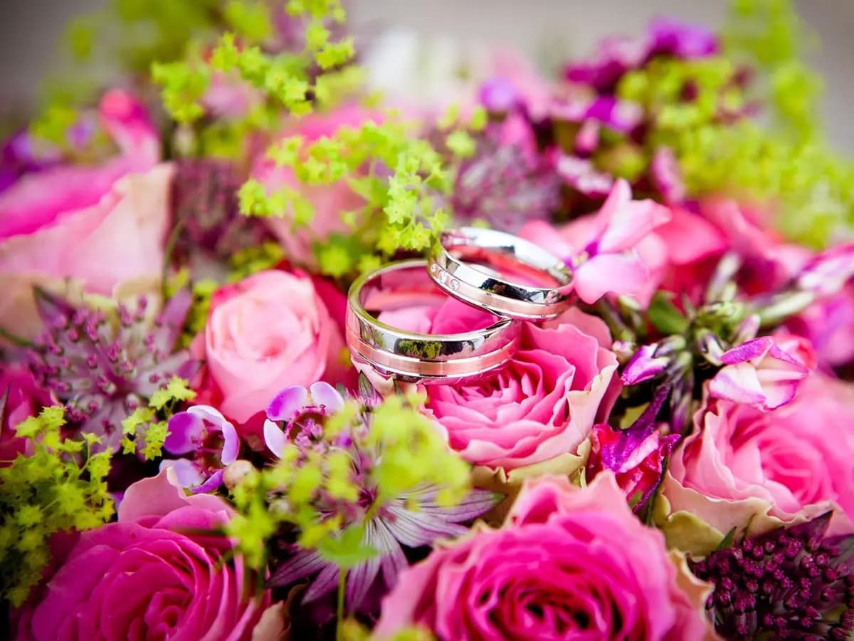 Two wedding rings resting on a bouquet of pink roses and purple flowers