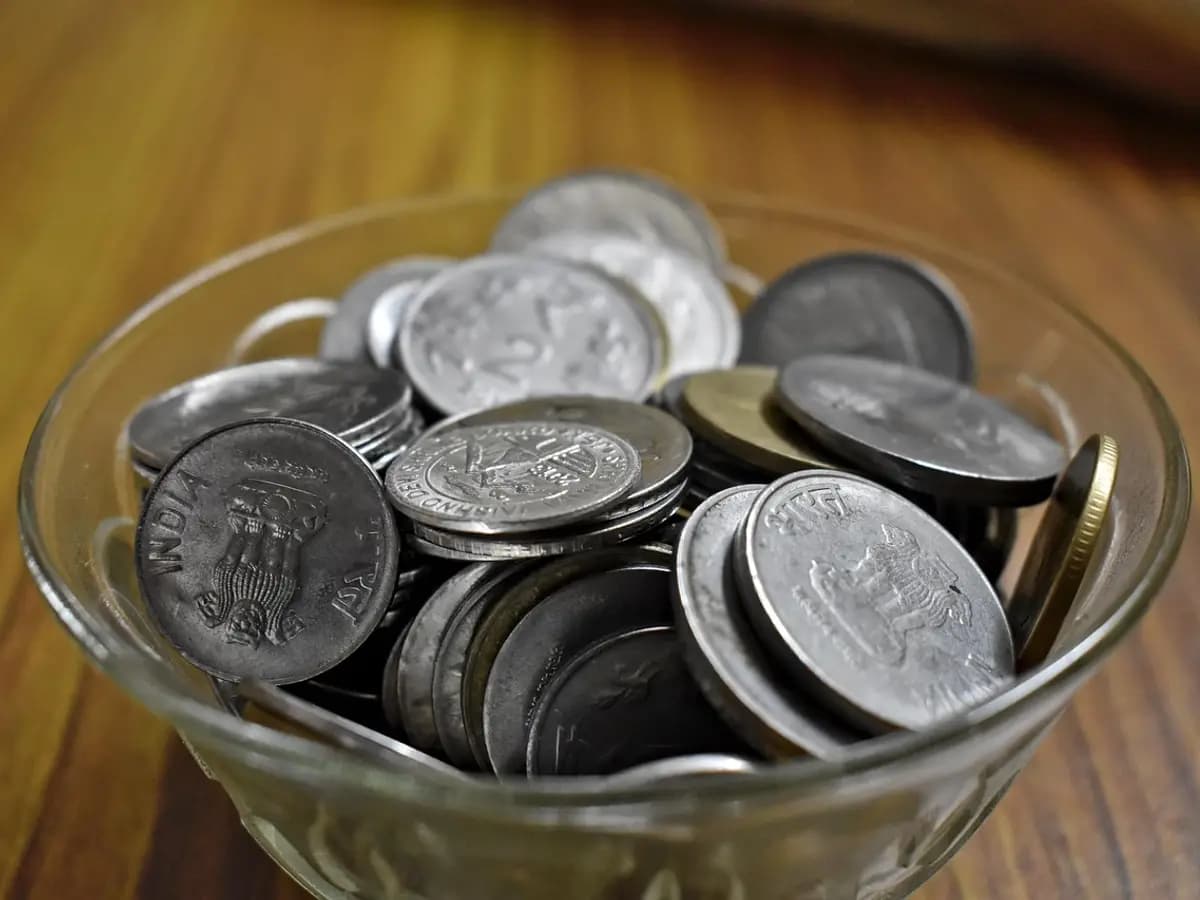 A glass bowl full of Indian rupee coins on a wooden table