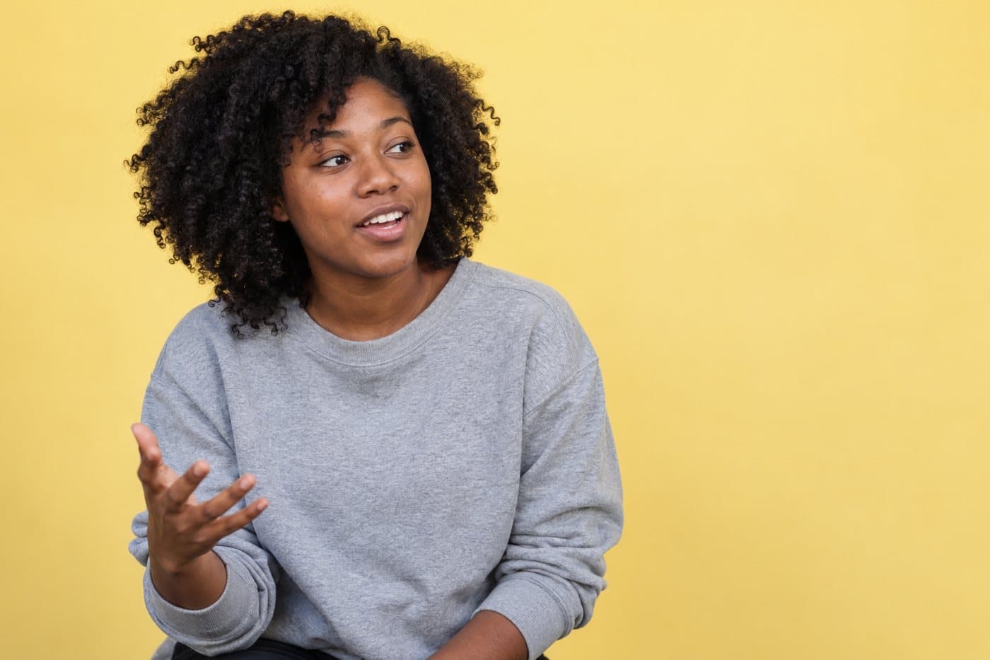 Example customer, a woman in a grey sweatshirt against a yellow backdrop, mid-sentence.